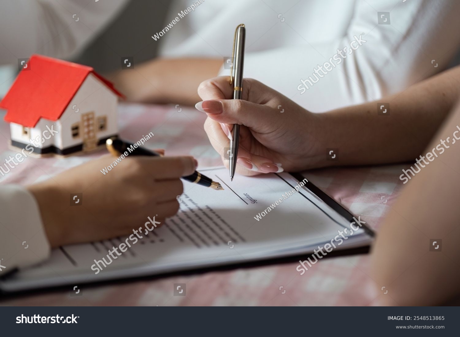 Stock photo signing real estate contract with model house on table close up of hands and pen 2548513865